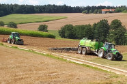 Traktor mit Güllefass fährt vor einem Traktor mit Pflug über ein Feld