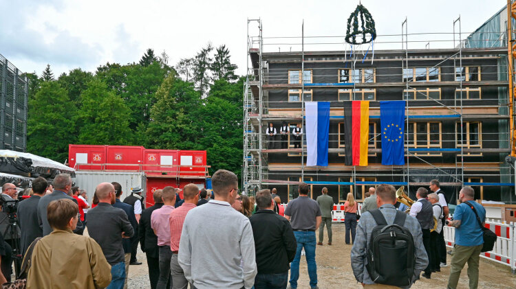 Personen stehen vor einem mit Gerüst eingeschalten mehrstöckigen Gebäude 